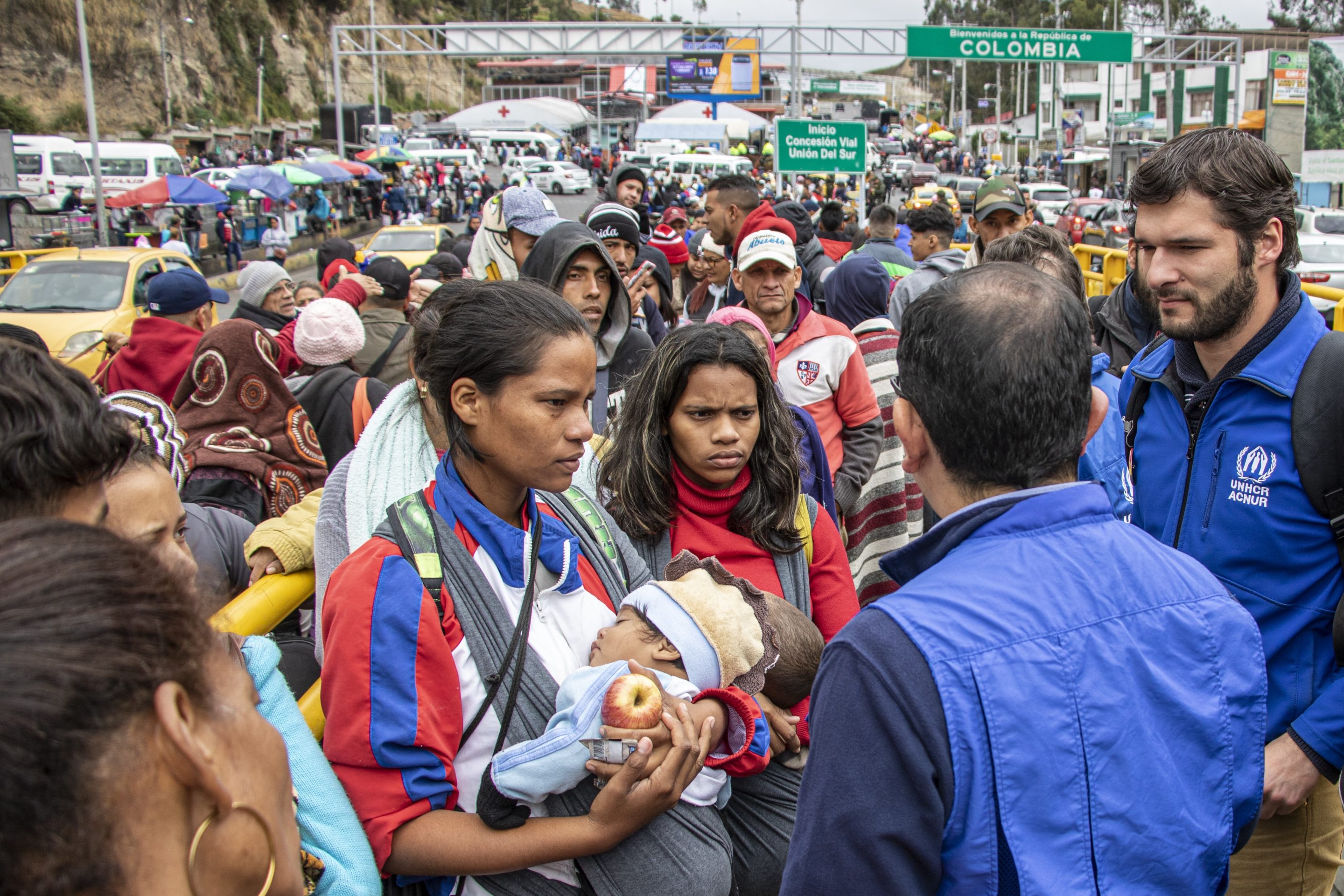 A crowd of people speaking to UNHCR staff on a bridge