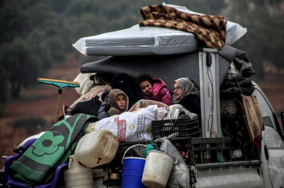 Family sitting in the back of a truck with their belongings piled up in Syria.