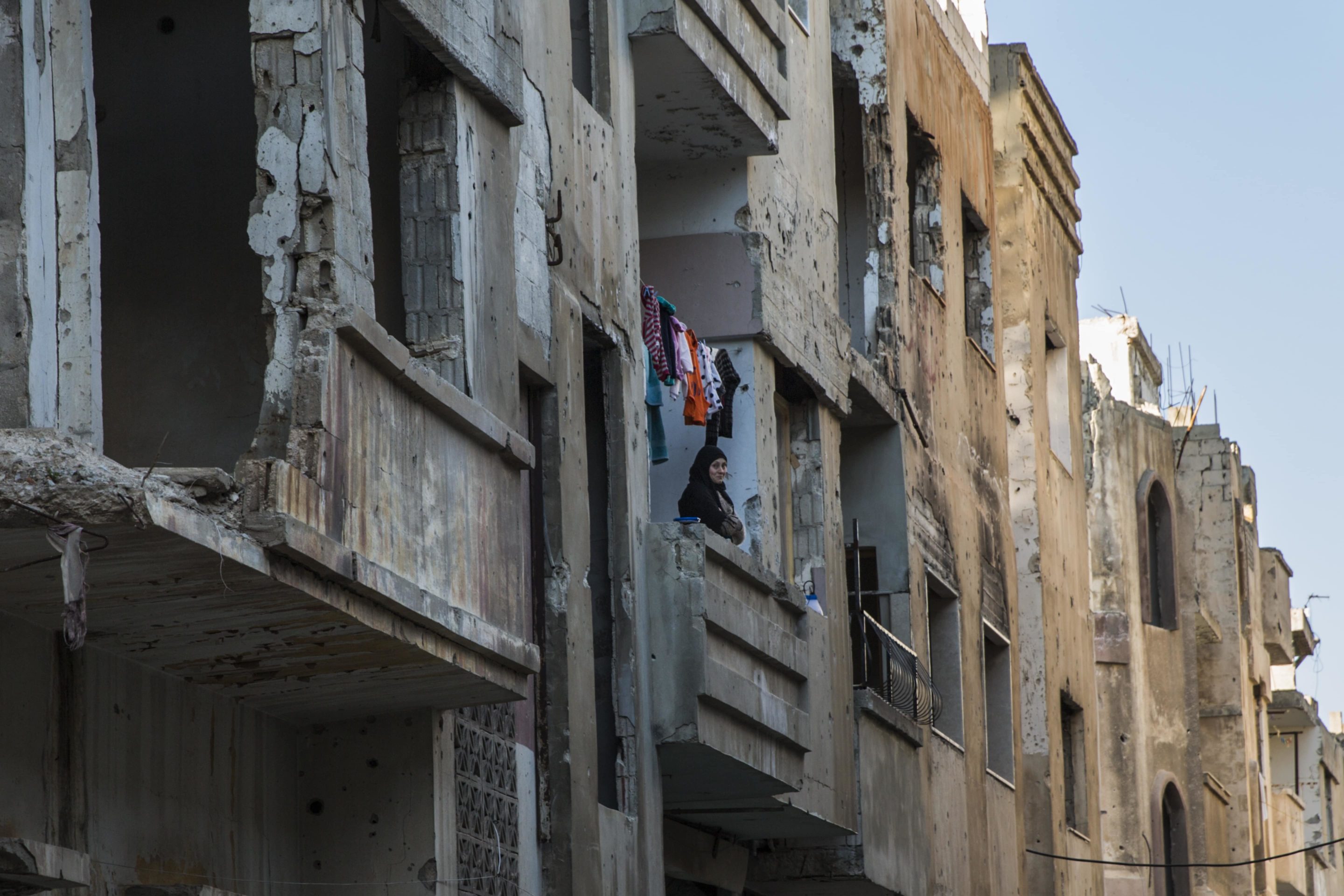 A syrian woman stands on a balcony of a building in ruins