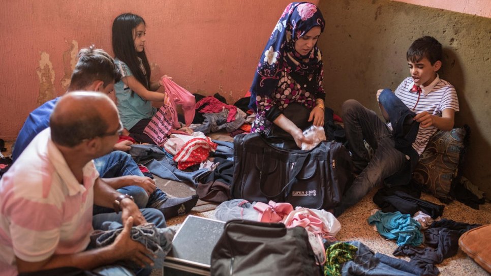 Zain, right, sits by his mother Nour as his family pack for their move to Norway.