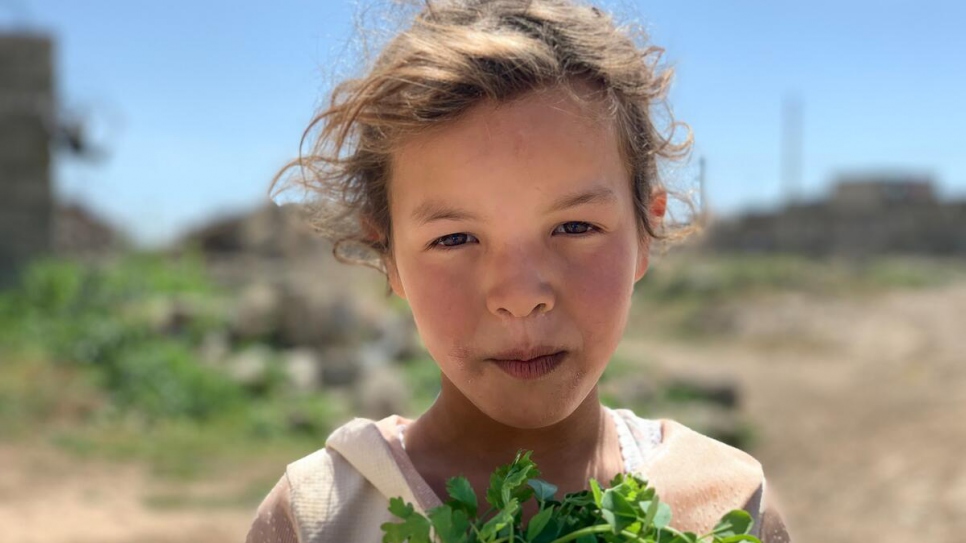 Une jeune fille porte un bouquet de brins de coriandre devant sa maison endommagée dans un village près de Mossoul.  