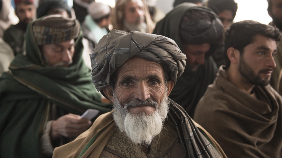 Mohammed Daud (au centre) attend avec d'autres Afghans dans la ville de Kandahar de recevoir la troisième tranche de son allocation en espèces du HCR pour construire une maison pour lui et sa famille (2 février 2020). 