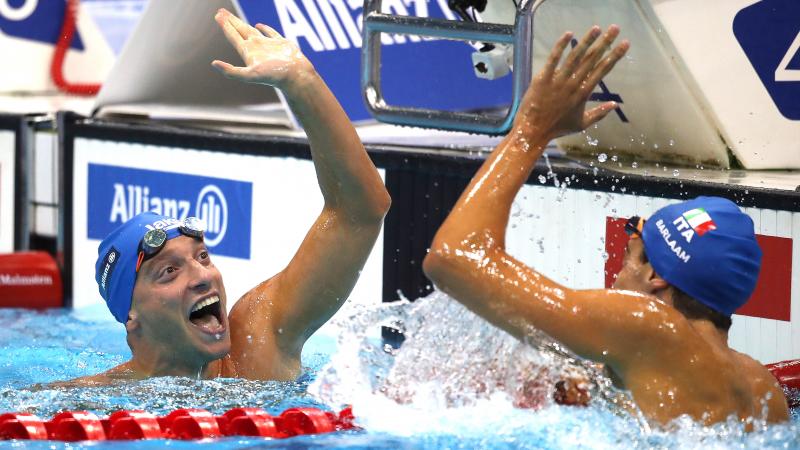 two male Para swimmers high fiving in the water