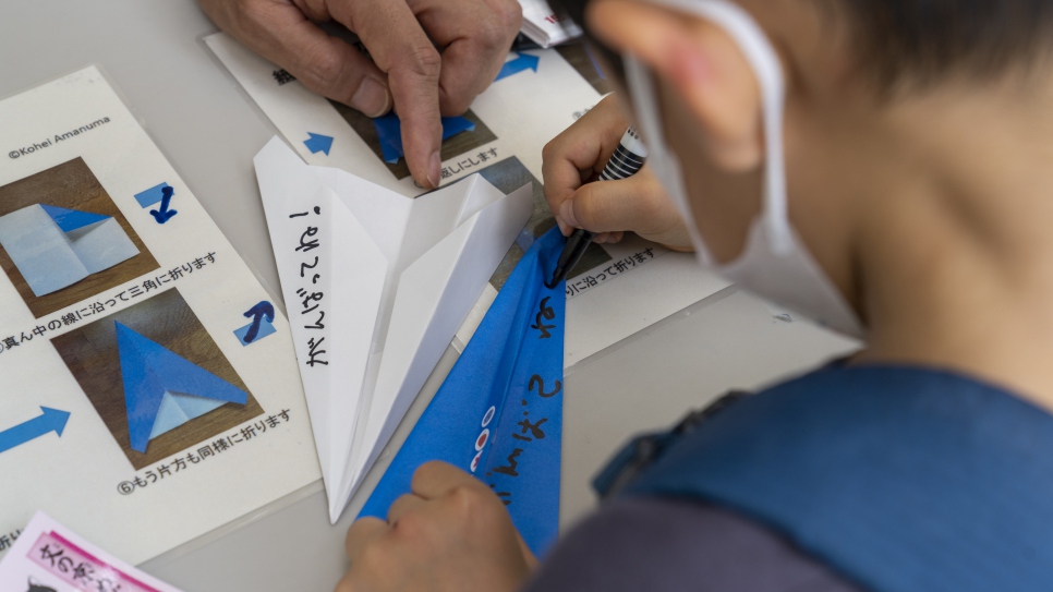 Un estudiante escribe mensajes para el Equipo Paralímpico de Atletas Refugiados en aviones de papel en Bunkyo, Japón.