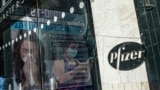 FILE - An ad for COVID-19 testing reflects on glass at a bus stop, as pedestrians walk past Pfizer world headquarters in New York, Nov. 9, 2020.