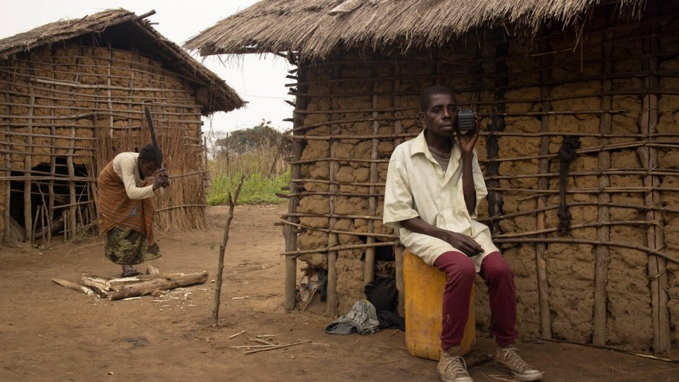 Damas Ngueste listens to the radio while his wife Marie chops wood to make a fire for cooking. 