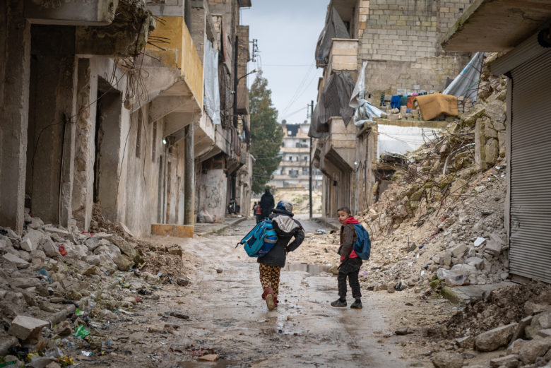 Children walk through an alley way in ruins.