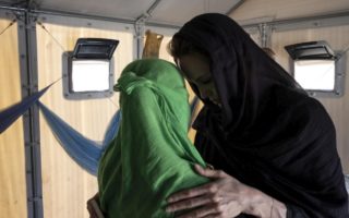 Two ladies in head scarves are standing face to face and providing each other support