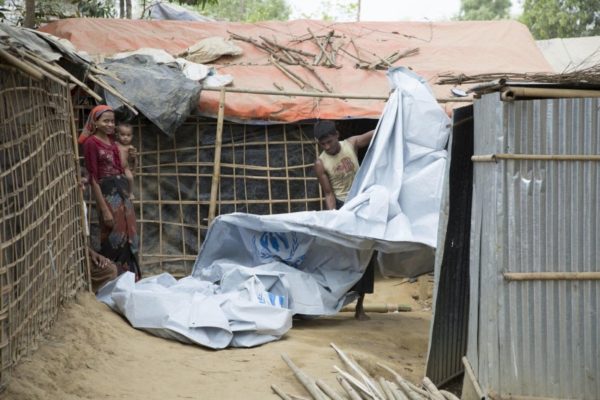 A man unravels a large white tarp while a woman holding a baby looks on