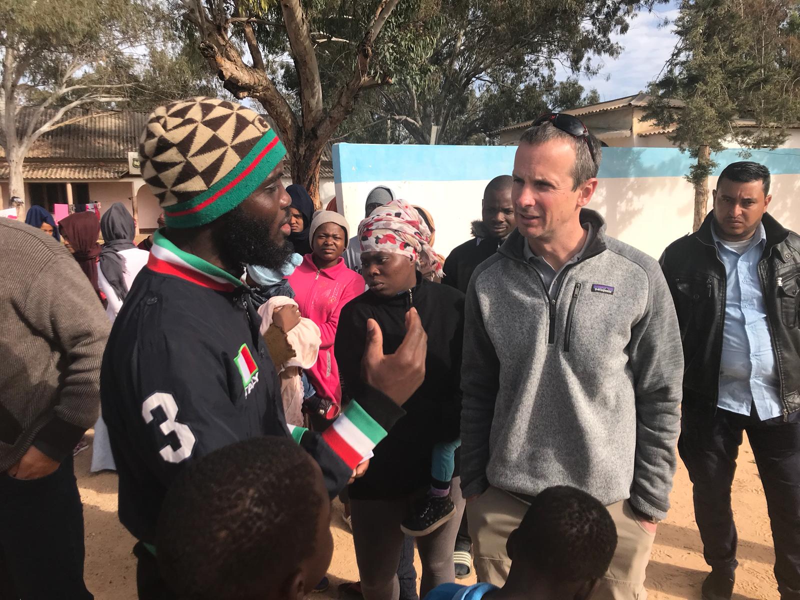 A man speaks to another man who is wearing a colourful hat