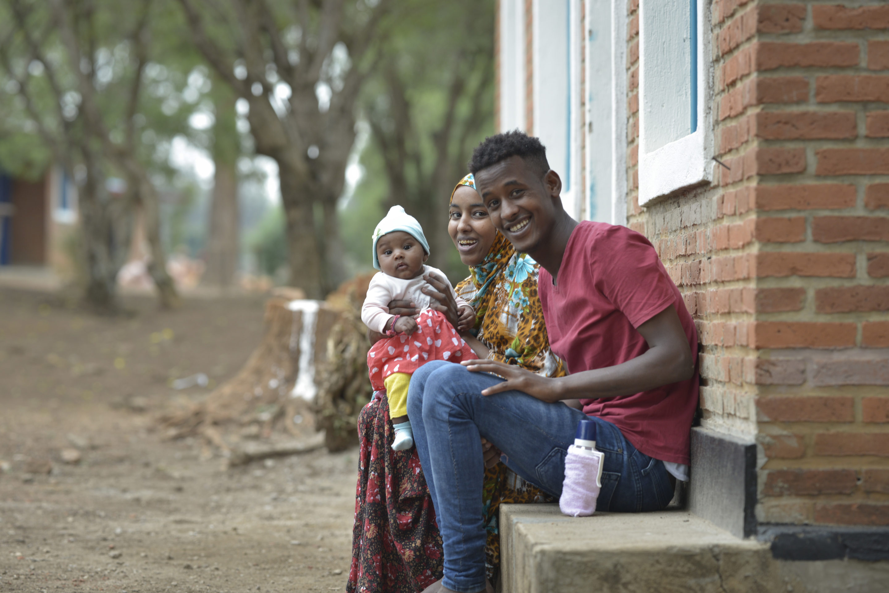 A young family sits on the steps of a brick building