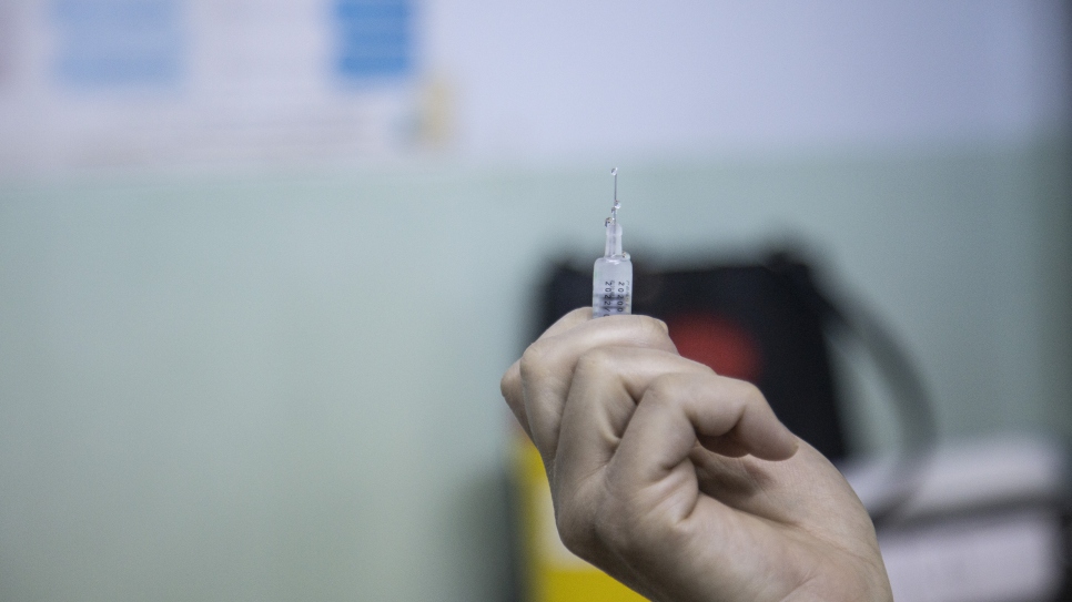 A medical worker prepares the COVID-19 vaccine to be administered to Iraqi refugee Raia Al Kabashi.