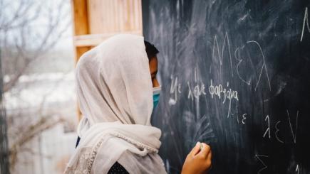 A person wearing a mask writes on a black board