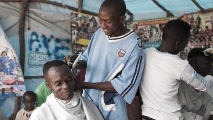 A man is giving another man a haircut at his barbershop