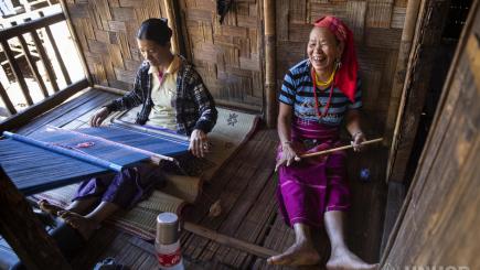 Two women sit together weaving