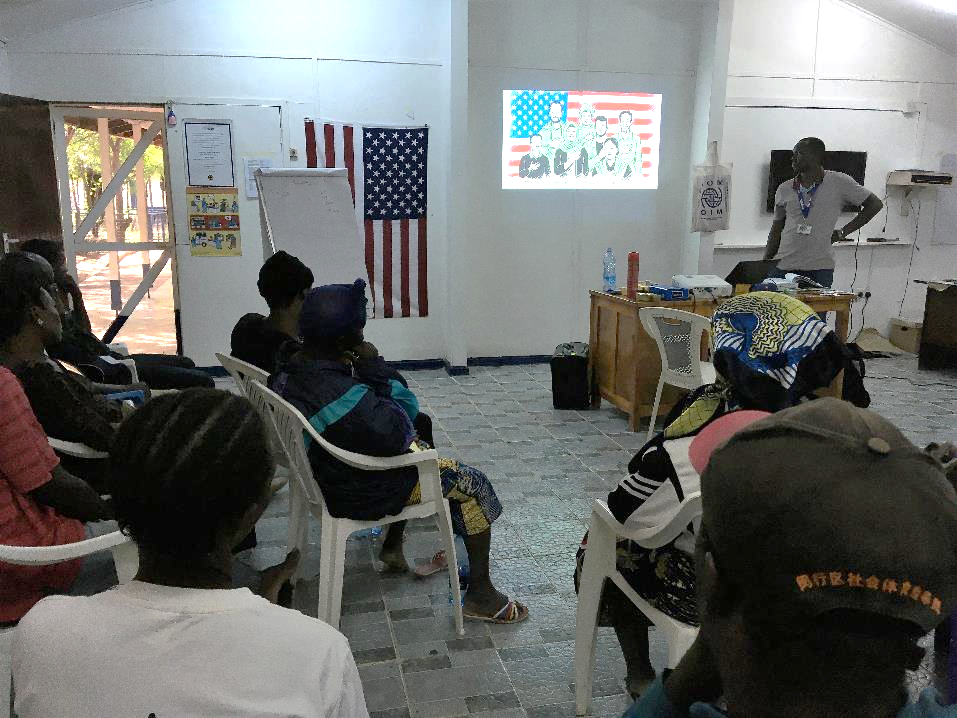 People seating on chairs in a room, listening to someone giving a presentation.