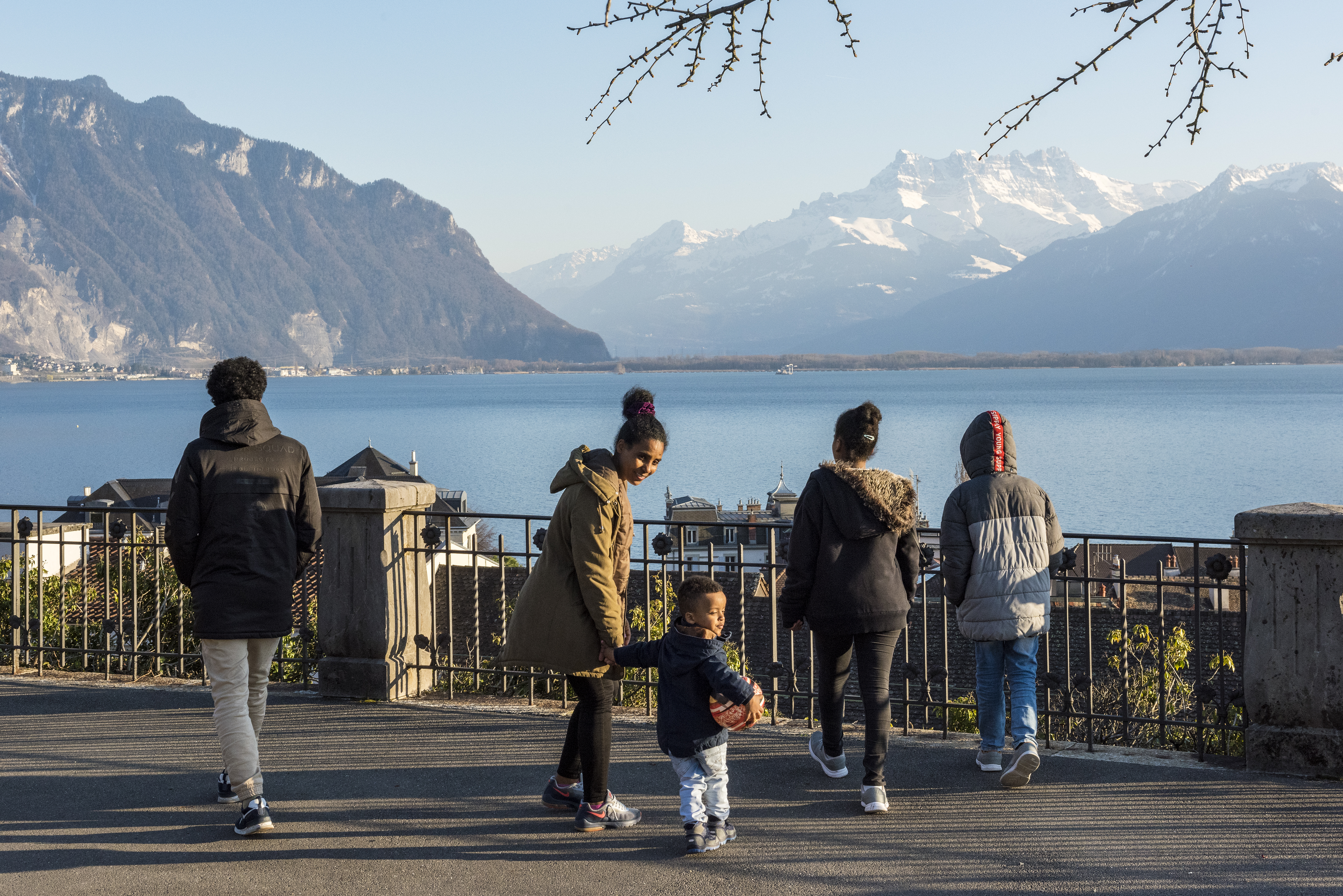 A family walks by a lake. Mountains in the background.