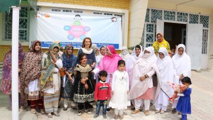 A group od women and children stand in front of a healthcare facility