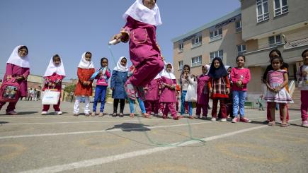 A girl jumps high over a skipping rope while others watch around. 