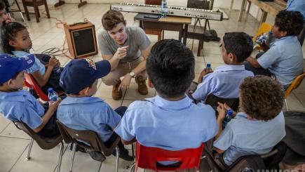 A group of children sit around their music teacher.