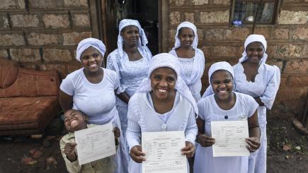 A group of people face the camera smiling holding up birth certificates