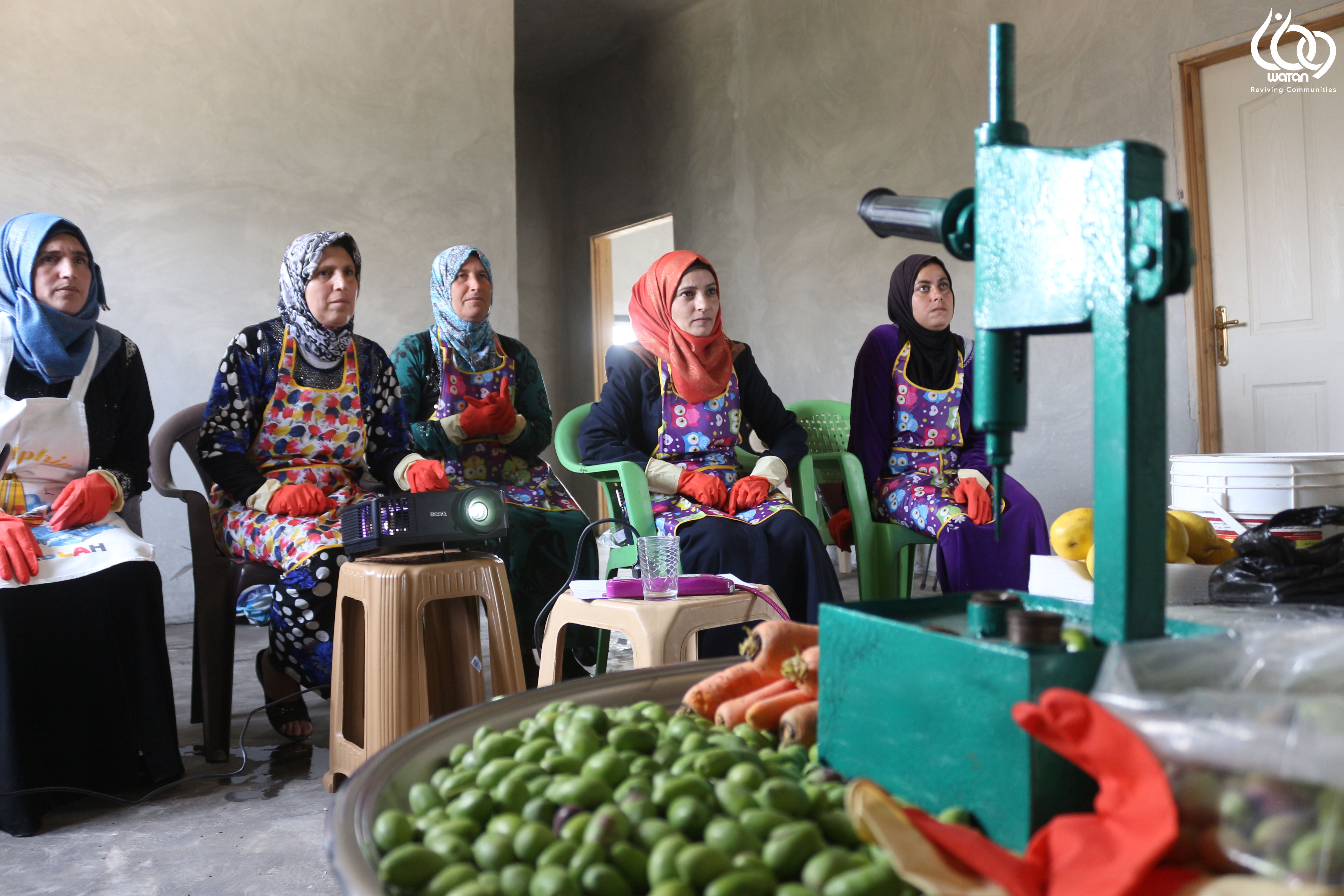 Five women are sitting together the are watching what a projector is showing. Olives can be seen on the foreground.