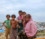 Cover Page - CCCM Case Studies 2016 - 2019. Four children stand smiling behind a woman seated on a hill. They are in Cox's Bazar