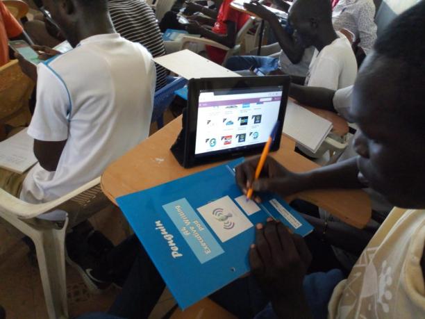 Student writing in his notebook while the digital platform is open