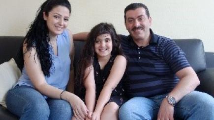 A woman, man and a child smiling at the camera sitting in a couch. 