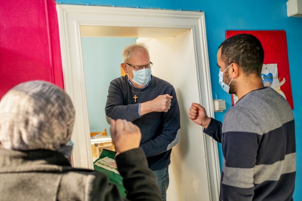 Two men wearing masks fist bump, one of them is a priest