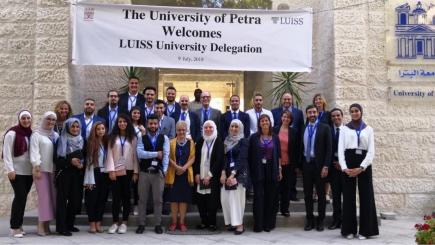 A group of people looking at the camera underneath a sign that says "The University of Petra Welcomes Luiss University Delegation 9 july 2018"