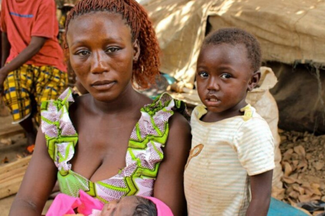 Deze moeder uit de Centraal-Afrikaanse Republiek (CAR) zit met haar kinderen naast haar geïmproviseerde onderkomen in het dorp Ndu, in de DR Congo. © UNHCR/Fabien Faivre