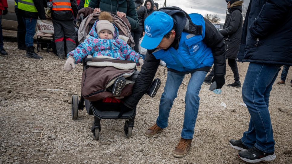 Batyr Sapbyiev, agent de protection du HCR, aide une mère et son enfant à se diriger vers les bus en attente au poste frontière de Palanca en Moldavie. 