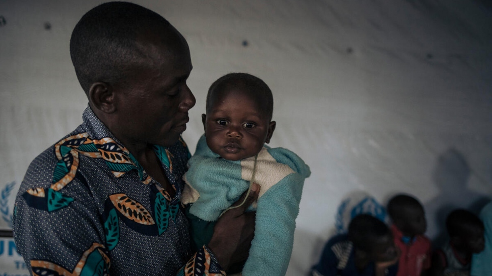 Firmin porte son fils alors qu'ils attendent d'embarquer sur un vol au départ de Gbadolite, dans le nord de la République démocratique du Congo, à destination de la République centrafricaine.  