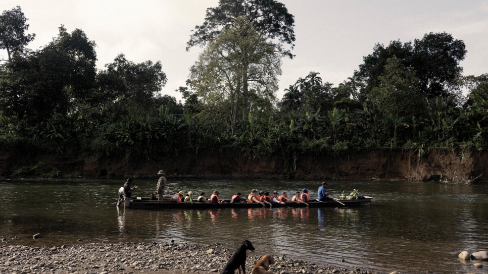Refugees and migrants sit in a canoe on the Membrillo River while an officer with Panama's National Border Service registers them.