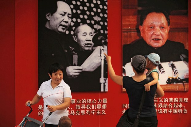 A mother (C) shows her child pictures of former communist party leaders Mao Zedong (top L) and Deng Xiaoping (top R) in Ditan Park in Beijing, June 28, 2011.