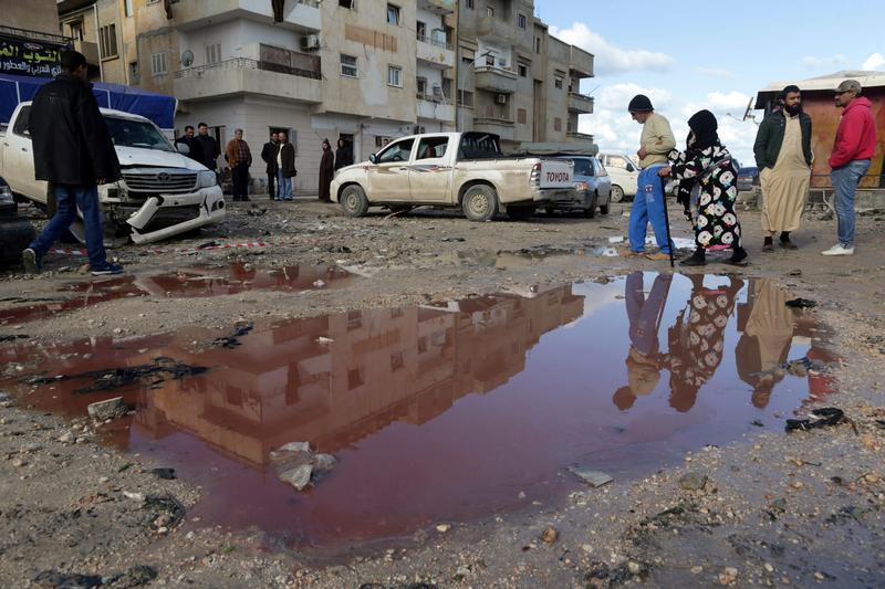 People walk near a puddle of water mixed with blood at the site of twin car bombs near a mosque in the Salmani neighborhood of Benghazi that resulted in scores of deaths and injuries, Libya, January 24, 2018.