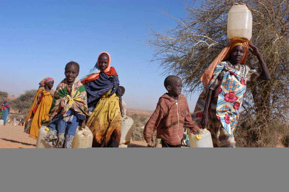 لاجئون في طريقهم إلى صنبور المياه في مخيم طولوم، يحملون معهم أوعية لنقل المياه لتلبية احتياجاتهم اليومية. عانت المفوضية وشركاؤها في العثور على مواقع للمخيمات تتوفر فيها إمدادات مياهٍ تكفي عشرات آلاف اللاجئين في المنطقة الصحراوية. (19 مارس، 2004).