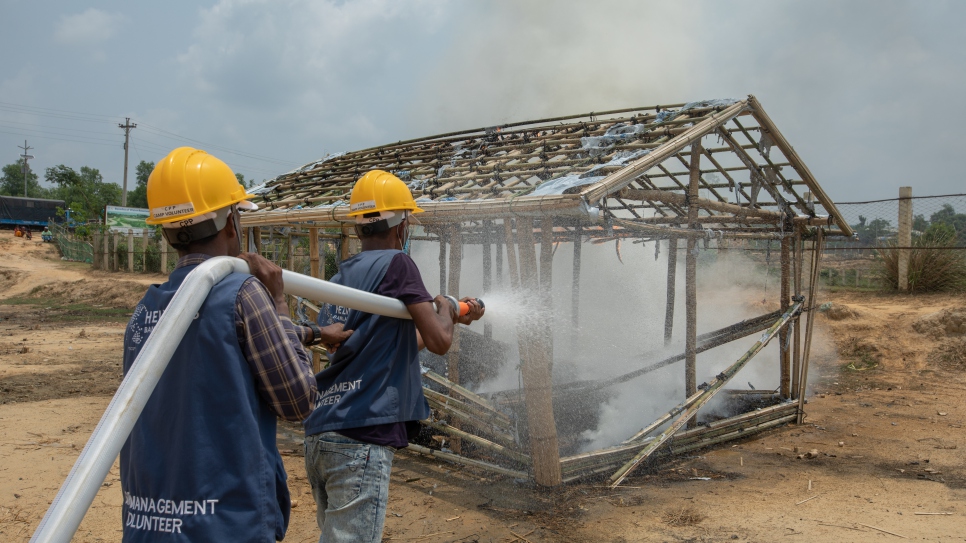Rohingya refugee volunteers use a hose attached to a three-wheeled fire truck to extinguish a fire during a training drill.