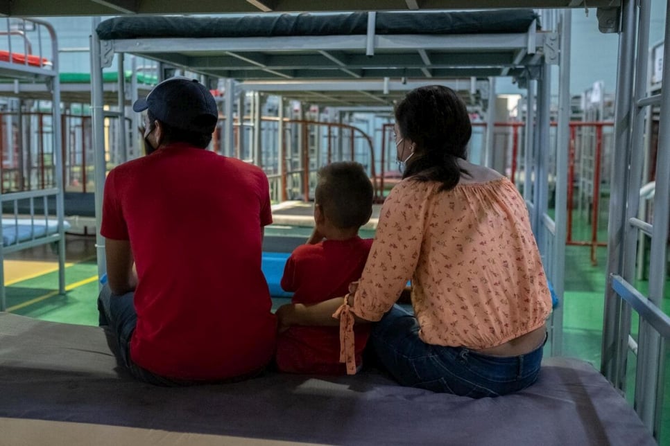 Honduran returnees sitting on a bed in the Kiki Romero gymnasium, a space enabled by the local government to provide care to people under Title 42.