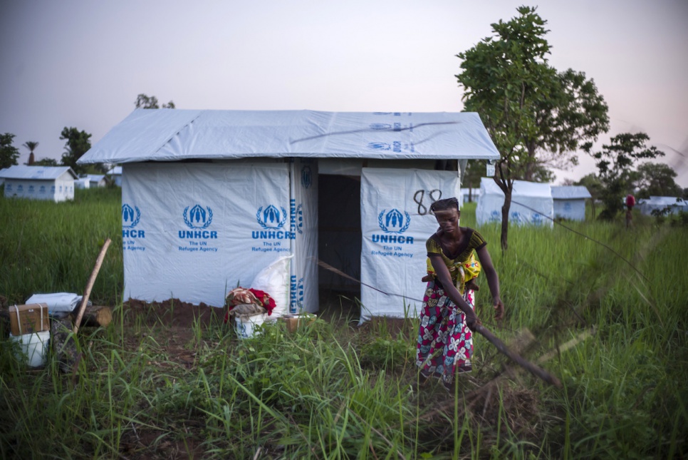 Tatiana clears brush in front of her family's new home in Bili camp. Six months ago, they left everything behind in the dash for safety.