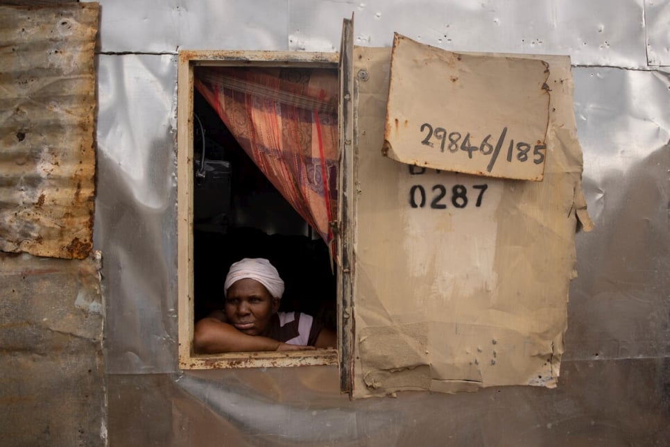 Bonisiwe regarde par la fenêtre du logement d'une pièce qu'elle partage avec trois de ses fils dans le bidonville de Mamelodi, près de Pretoria, en Afrique du Sud.