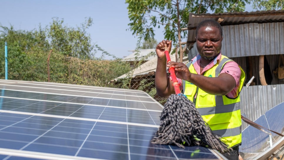 Vasco cleans the solar panels that power his mini-grid business at Kakuma camp.