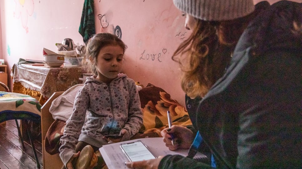 A UNHCR staff member speaks to Milana in her family's room.