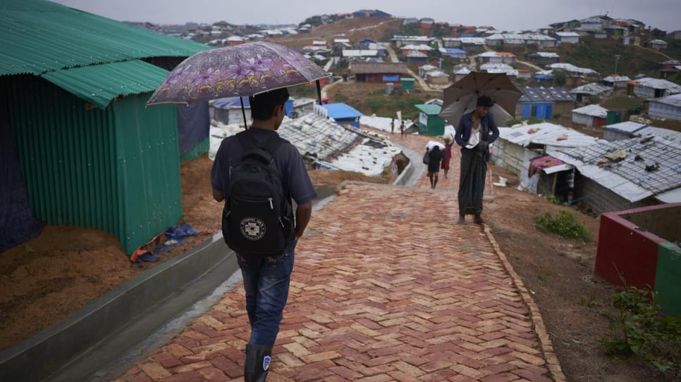 Community health worker and Rohingya refugee Shokat Ali, 26, left, walks down a paved footpath in Camp 4, Kutupalong Expansion Site for Rohingya refugees, Ukhia, Cox's Bazar District, Bangladesh.