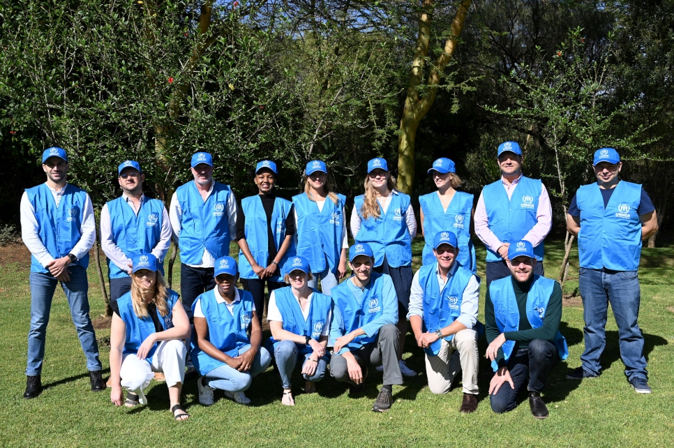 A group of about 15 people wearing blue UNHCR vests smile for the camera