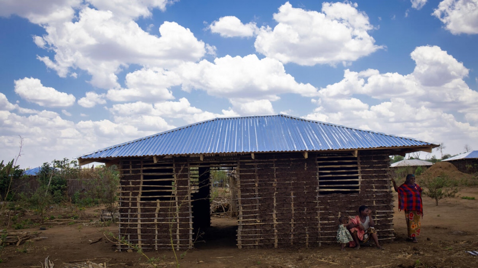 Anastasia (in red), 32, stands in front of her family's new home. Their previous shelter was severely damaged by  Cyclone Gombe.