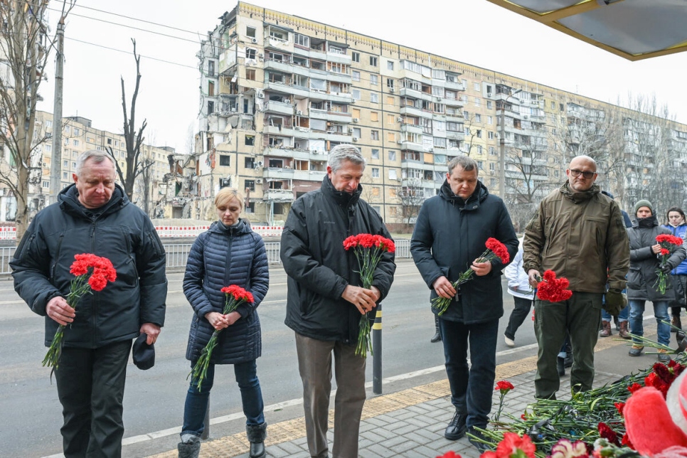 El Alto Comisionado Filippo Grandi (al centro), junto a representantes de las autoridades locales, coloca flores en un edificio residencial destruido durante un ataque con misiles el 14 de enero de 2023, en la ciudad de Dnipro, Ucrania.