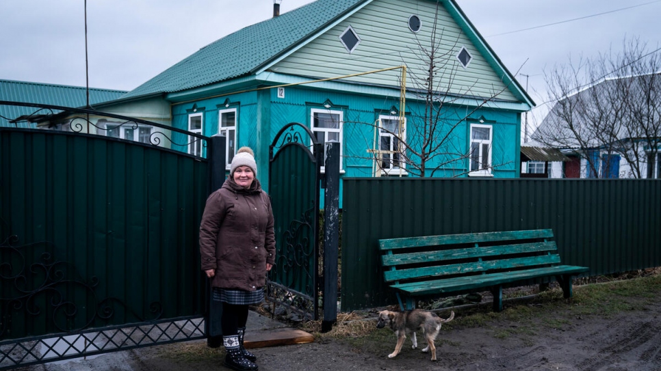 Olena frente a la casa de sus padres, cuyo tejado, puertas y ventanas fueron reparados por ACNUR después de sufrir daños.