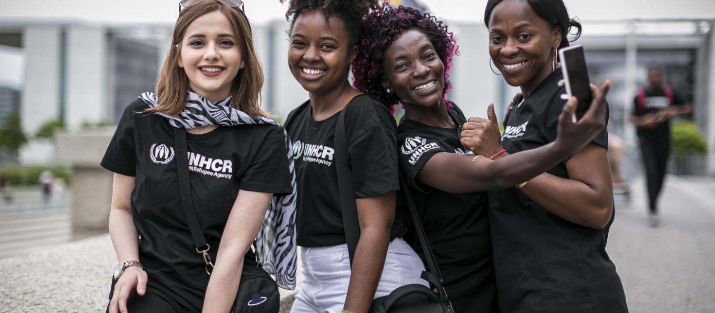 A group of four young women wearing UNHCR t-shirts smile for the camera 